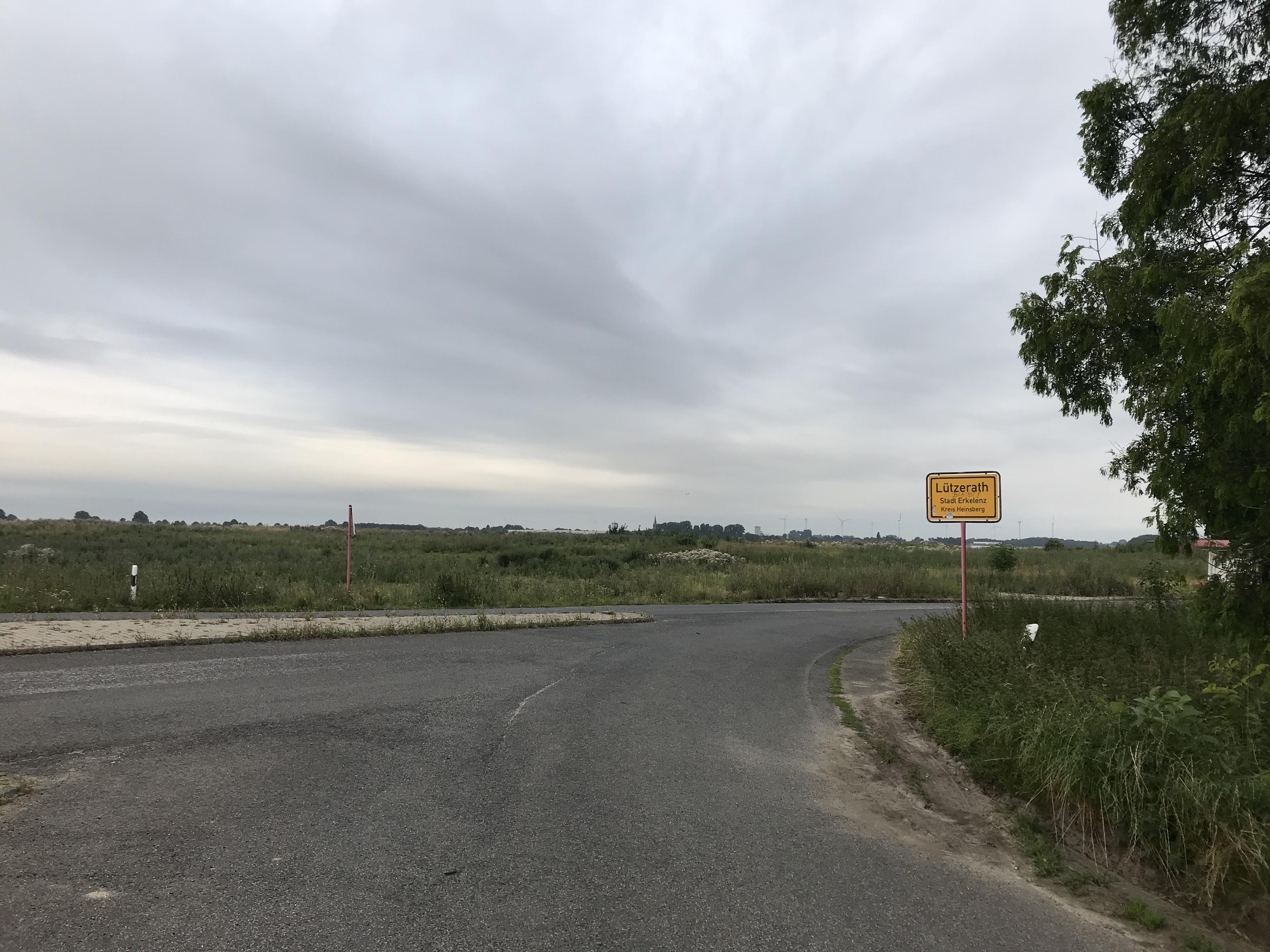 Sicht auf Ortsschild Lützerath mit Brache im Hintergrund