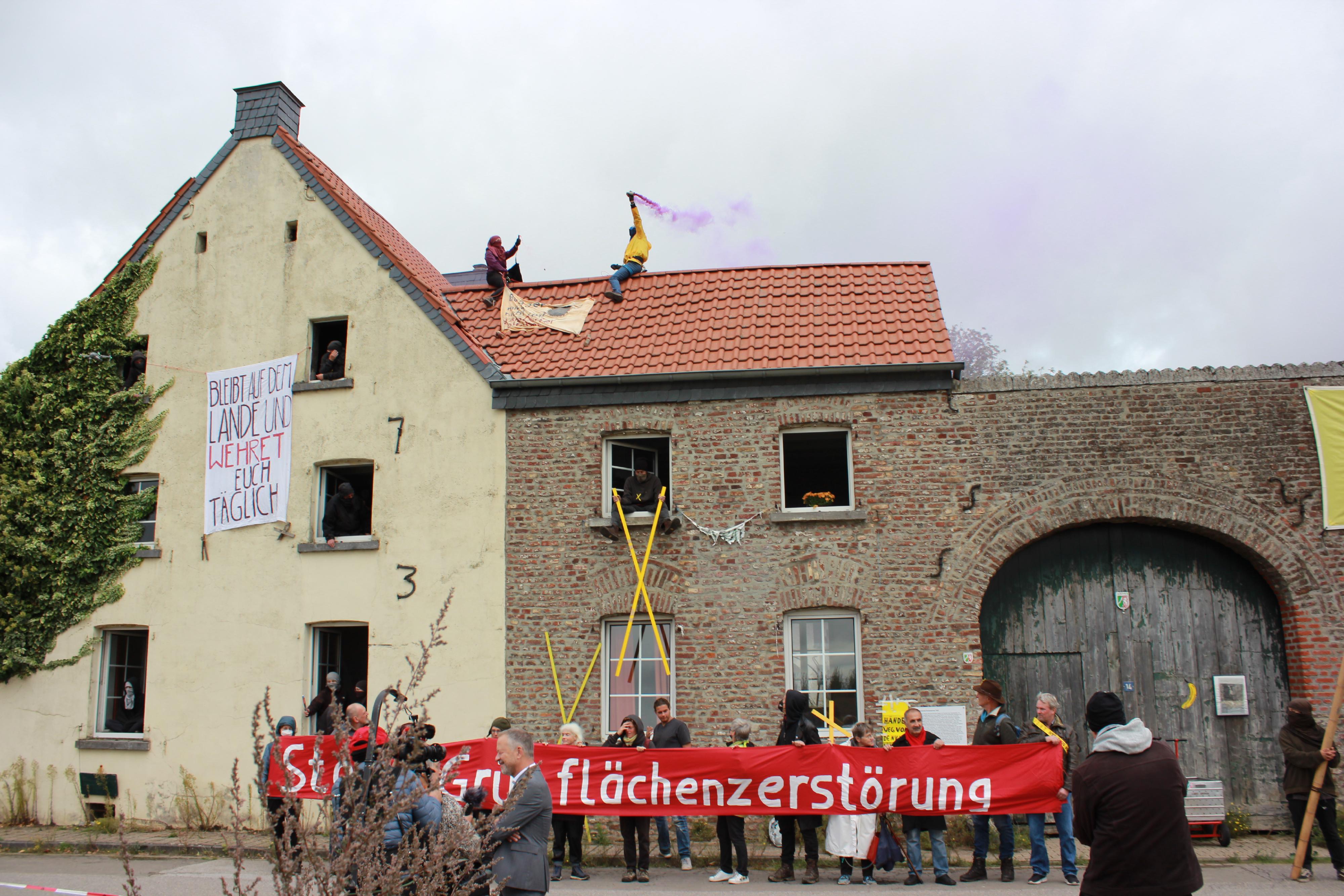 Hof von Eckardt Heukamp am 2. Okbober 2022, Tag, an dem er die Schlüssel an RWE übergeben musste. Menschen schauen aus den Fenstern und halten ein Banner mit der Aufschrift: Stoppt Grünflächenzerstörung