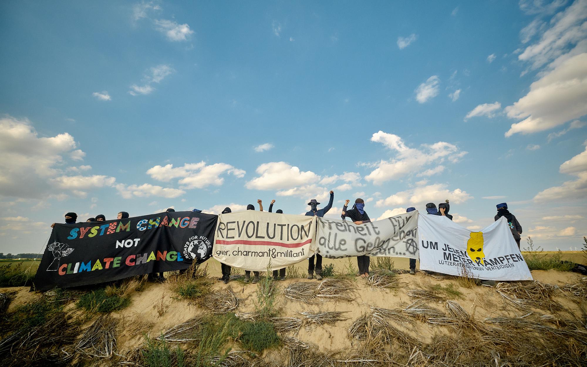 Foto von der FFF-Demo am 03.09.2022. Aufgenommen an der Kante, mehrere Menschen haben sich in einer Reihe aufgestellt, im Blick sind groß die bunten Banner mit Aufschriften wie: "System change not climate change" und "Um jeden Meter kämpfen – Lützerath offensiv verteidigen".