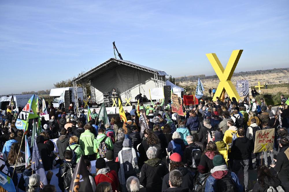 Bild der Demo vom 12. November 2022. Eine große Menschenmenge blickt auf die Bühne am Wendehammer. Im Hintergrund der Braunkohletagebau und am Horizont die im Dezember 2021 entwidmete Kirche von Keyenberg.