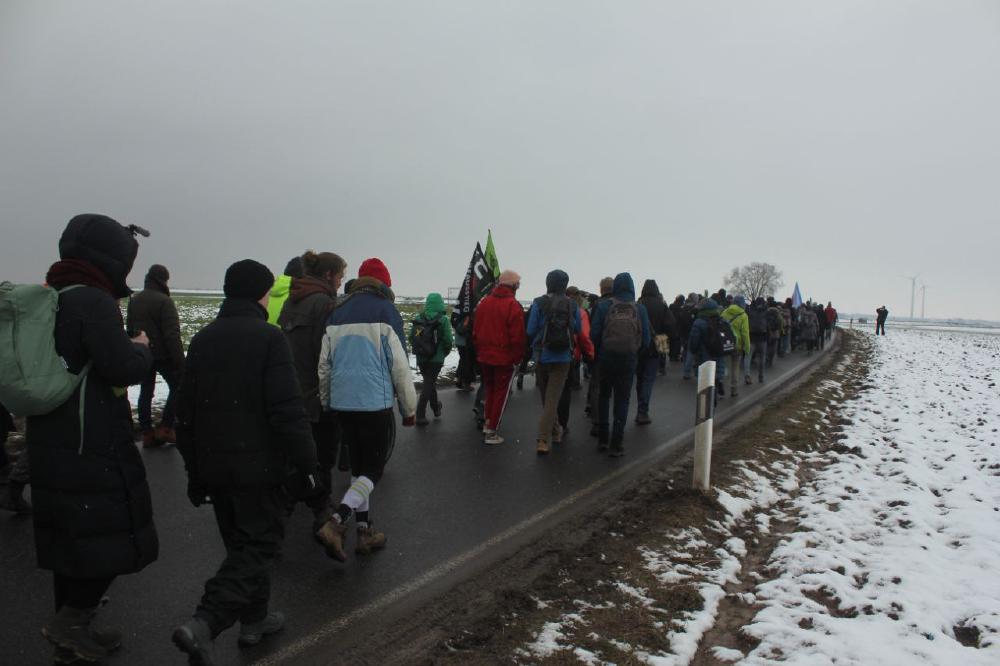 Bild vom Dorfspaziergang vom 22. Januar 2023. Ca 50 Menschen gehen von Keyenberg auf der Landstraße in Richtung Holzweiler. Links und rechts liegt Schnee.