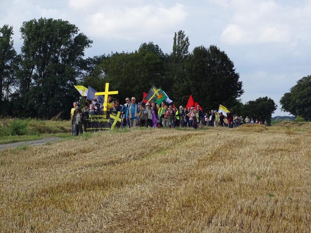 Ein Bild des Kreuzwegs 2021 von Gorleben nach Lützerath. Eine Menschengruppe, an der Spitze das gelbe Kreuz und ein Banner mit der Aufschrift Kreuzweg für die Schöpfung 2021. Ein Bild des Kreuzwegs 2021 von Gorleben nach Lützerath. Eine Menschengruppe, an der Spitze das gelbe Kreuz und ein Banner mit der Aufschrift Kreuzweg für die Schöpfung 2021.