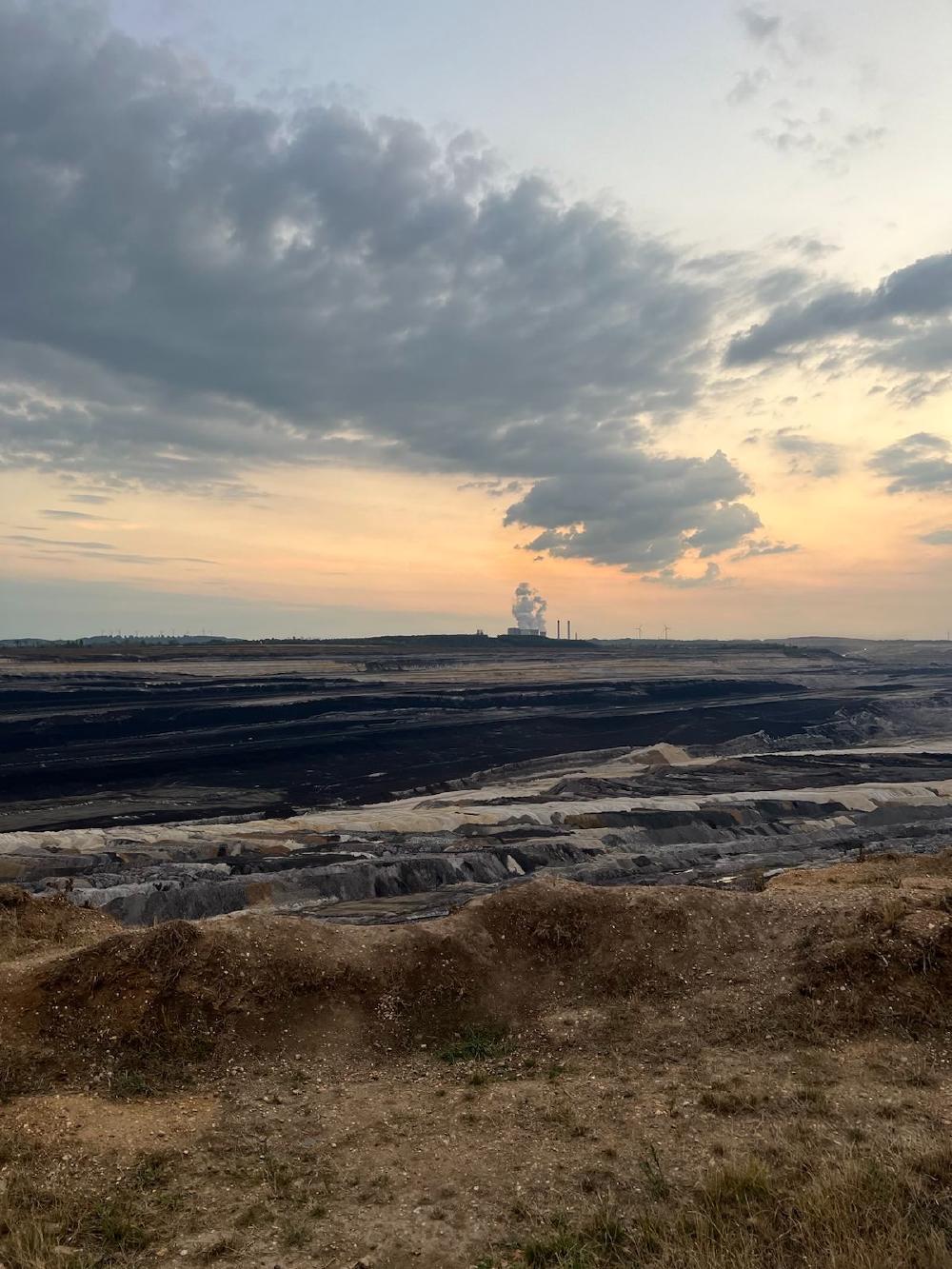 Foto vom Tagebau Inden. Ein großes Loch mit unterschiedlichen Erdschichten ist sichtbar. Im Hintergrund sind die qualmenden Kraftwerke zu sehen.